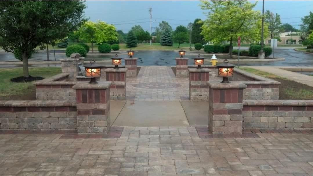 Stone walkway with lanterns leading to a garden path, flanked by brick walls and green trees.