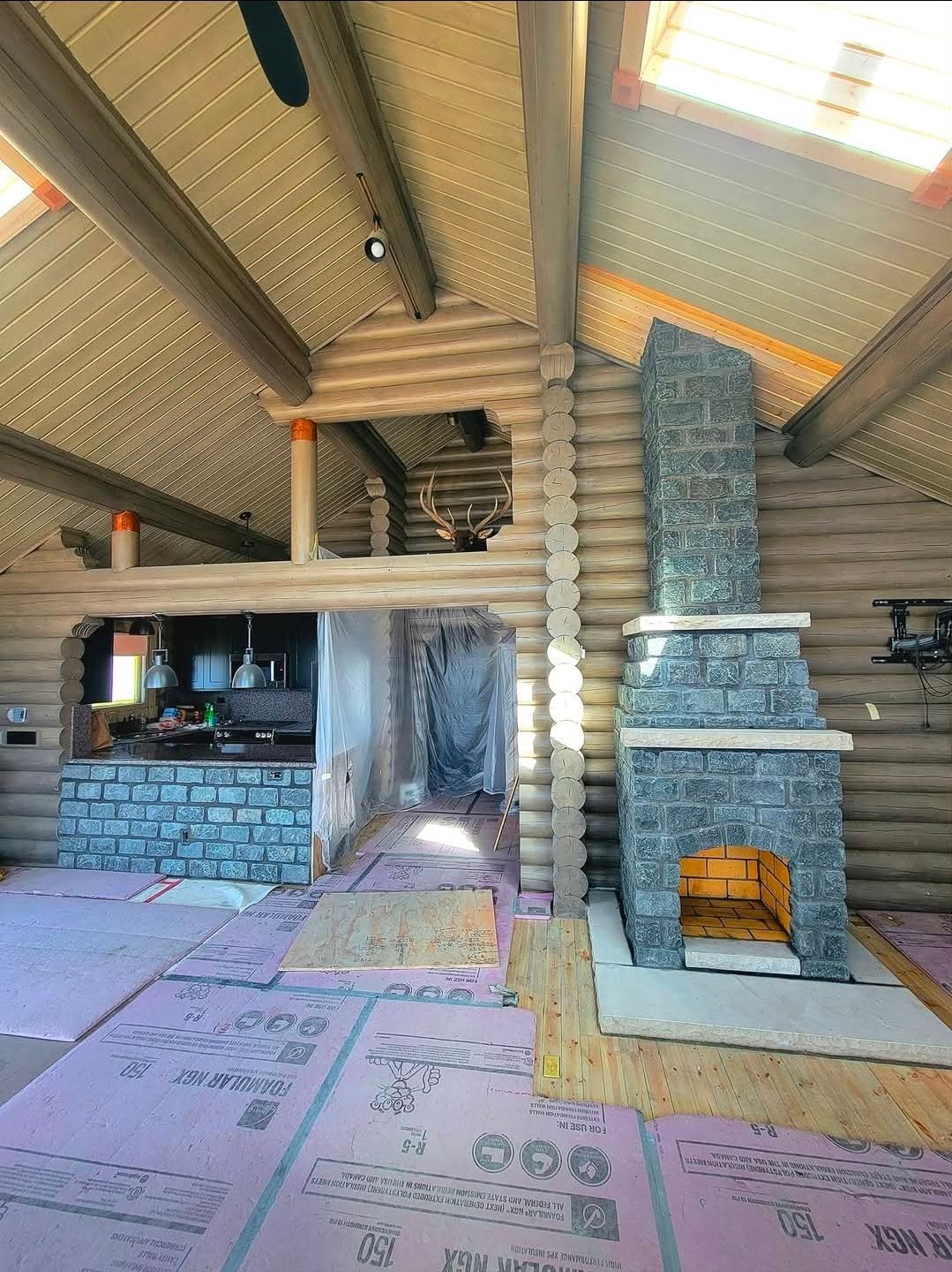 Rustic cabin interior with stone fireplace, wood beams, and unfinished pink floor under construction