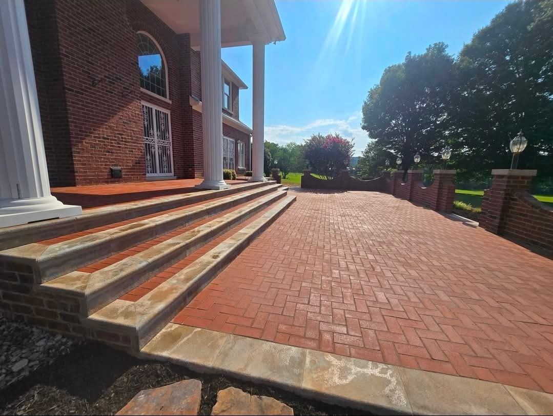 Brick courtyard and front steps leading to a columned building in bright sunlight