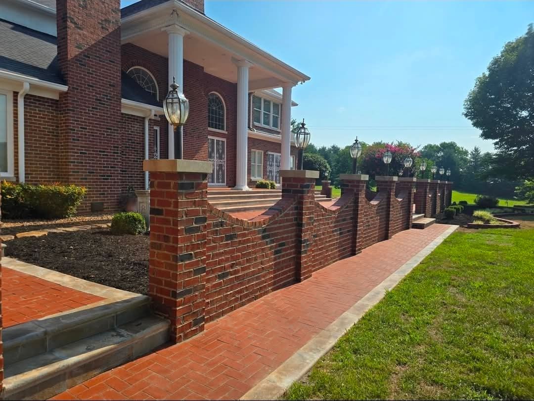 Brick house with white columns, red brick wall, and walkway beside a green lawn on a sunny day