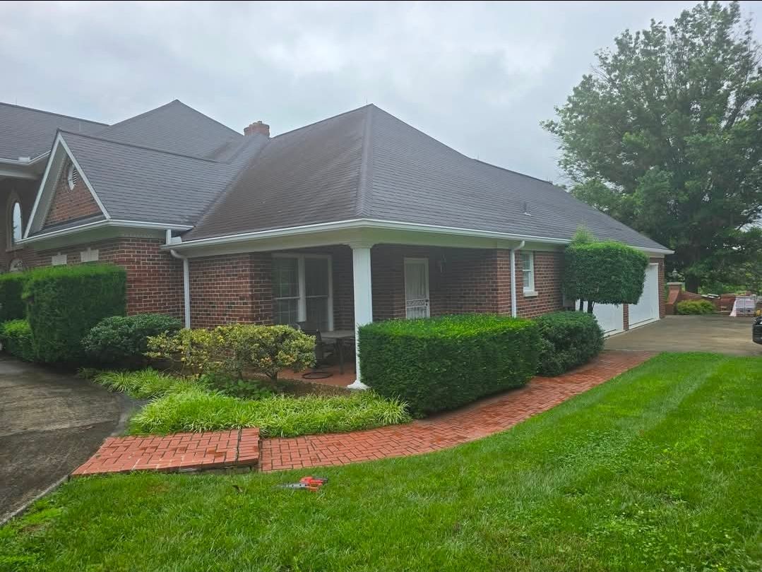 Brick house with dark roof, trimmed hedges, and green lawn on a cloudy day