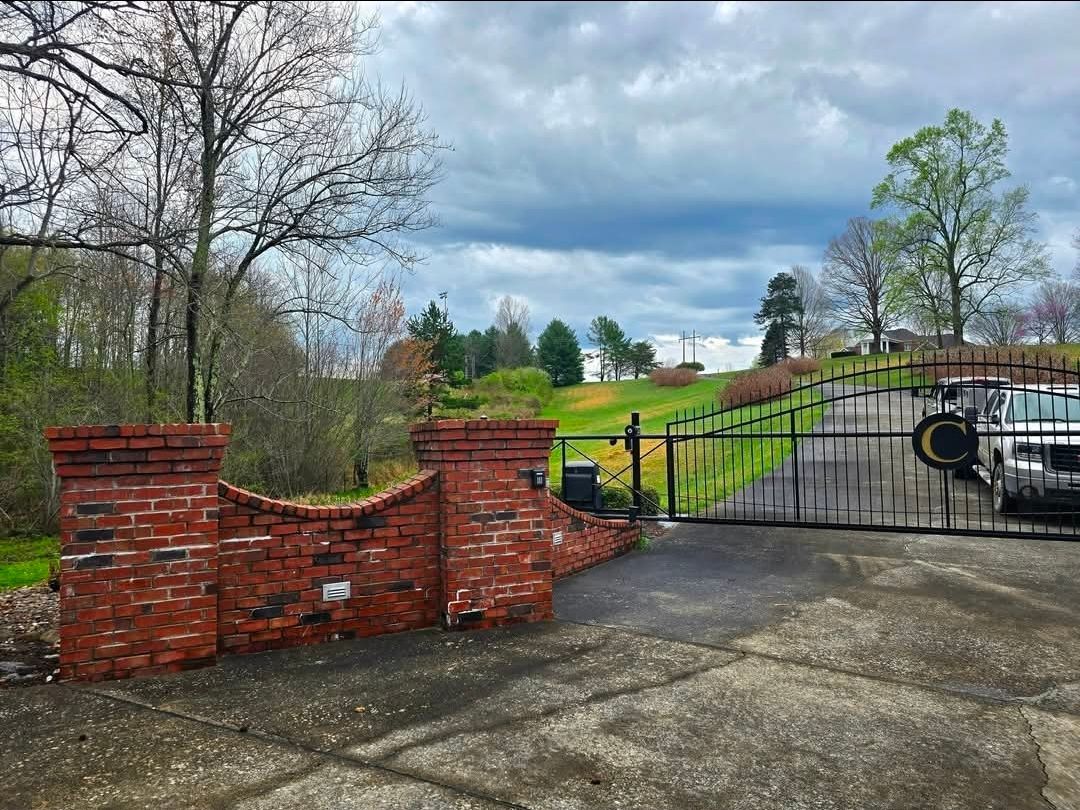 Brick gate beside a closed black metal gate, overlooking a driveway and cloudy rural landscape