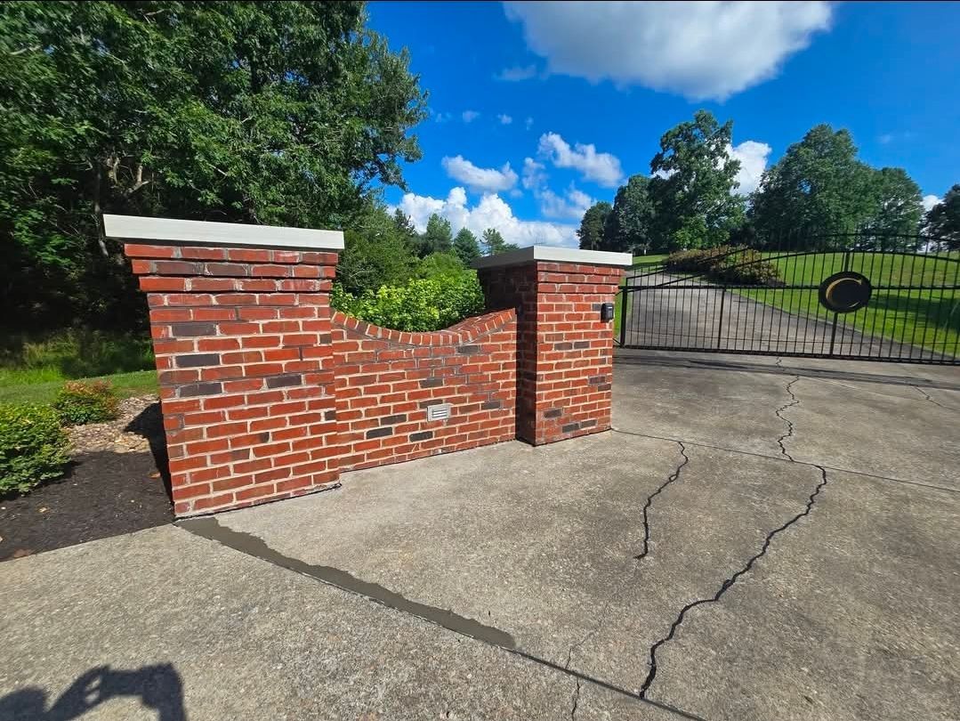 Brick retaining wall and pillars beside a cracked driveway under a blue sky.