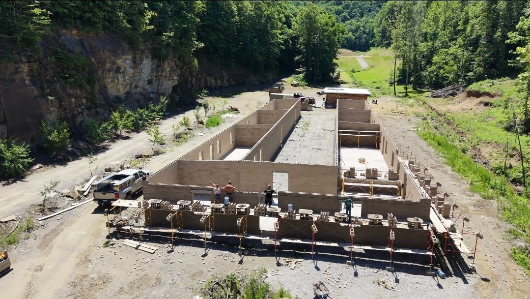 Partially built concrete foundation at an outdoor construction site, surrounded by trees and rocky terrain