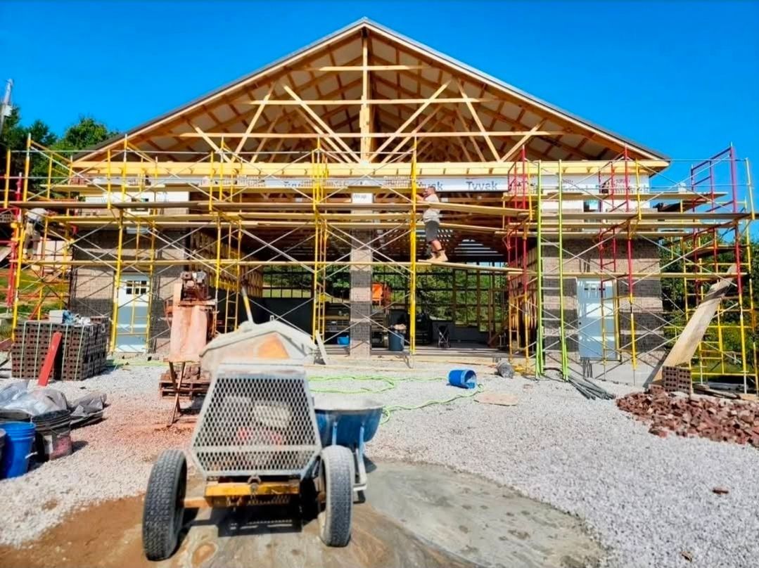 Construction site with a house under renovation, yellow scaffolding, and a utility vehicle in front