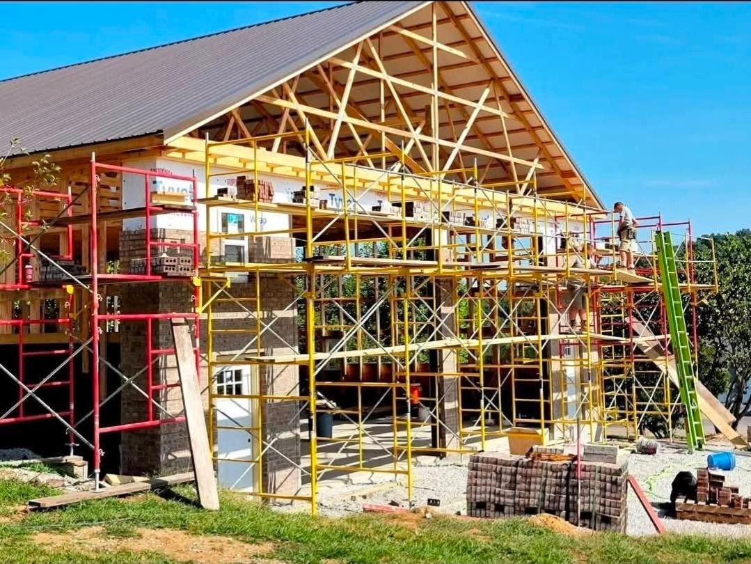 House under construction with red and yellow scaffolding and exposed wooden framing under a blue sky