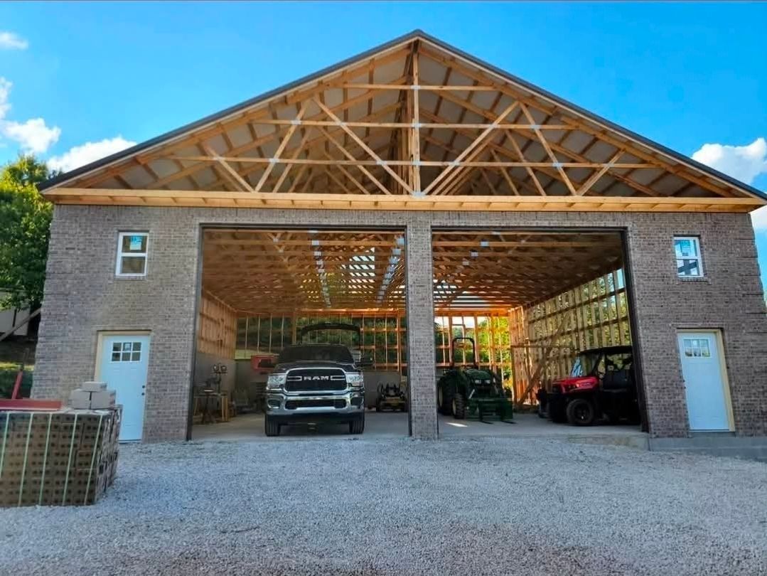 Open-sided wooden barn with two cars parked inside and gravel driveway in front