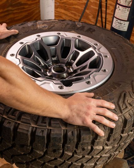 Gloved mechanic uses a lug wrench on a shiny alloy car wheel and tire, conveying careful, hands-on vehicle maintenance.