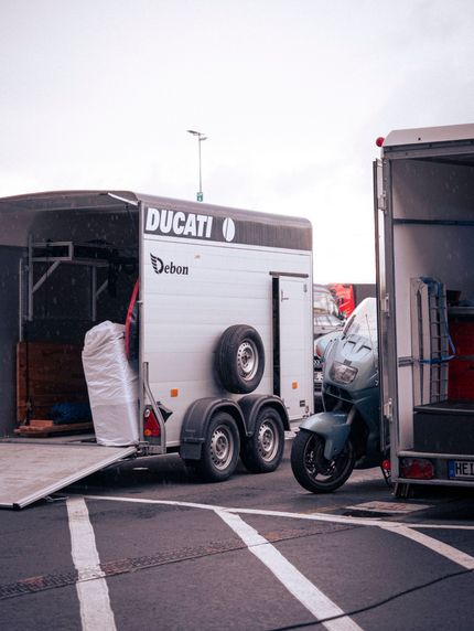 Close-up of two large black trailer tires with silver multi-hole rims and red hub centers beneath a metal truck trailer on asphalt.