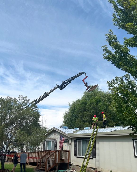 Workers in safety gear use a crane to lift branches over a house roof after storm damage.