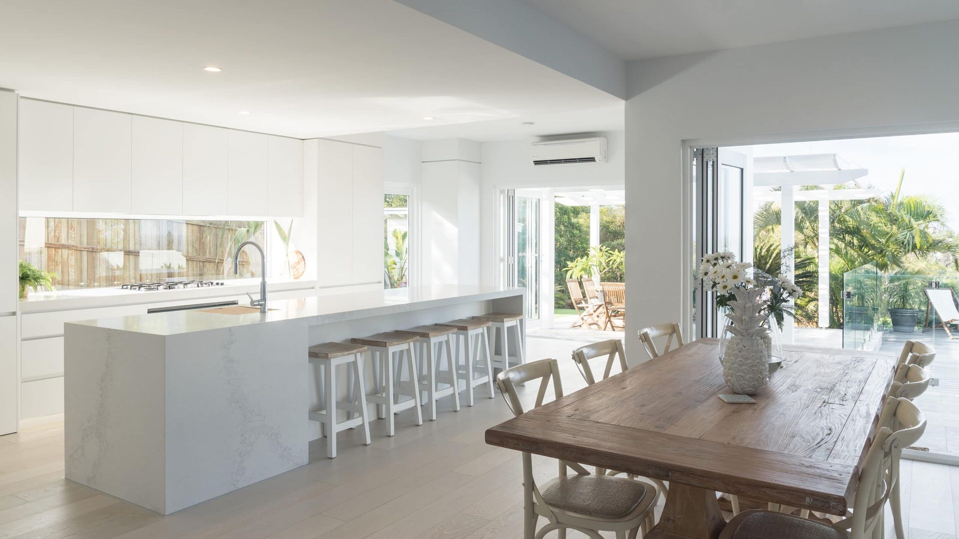 Bright White Kitchen With Large Island, Dining Table, and Open Doors to a Garden — Akyrah Kitchens in Gympie, QLD