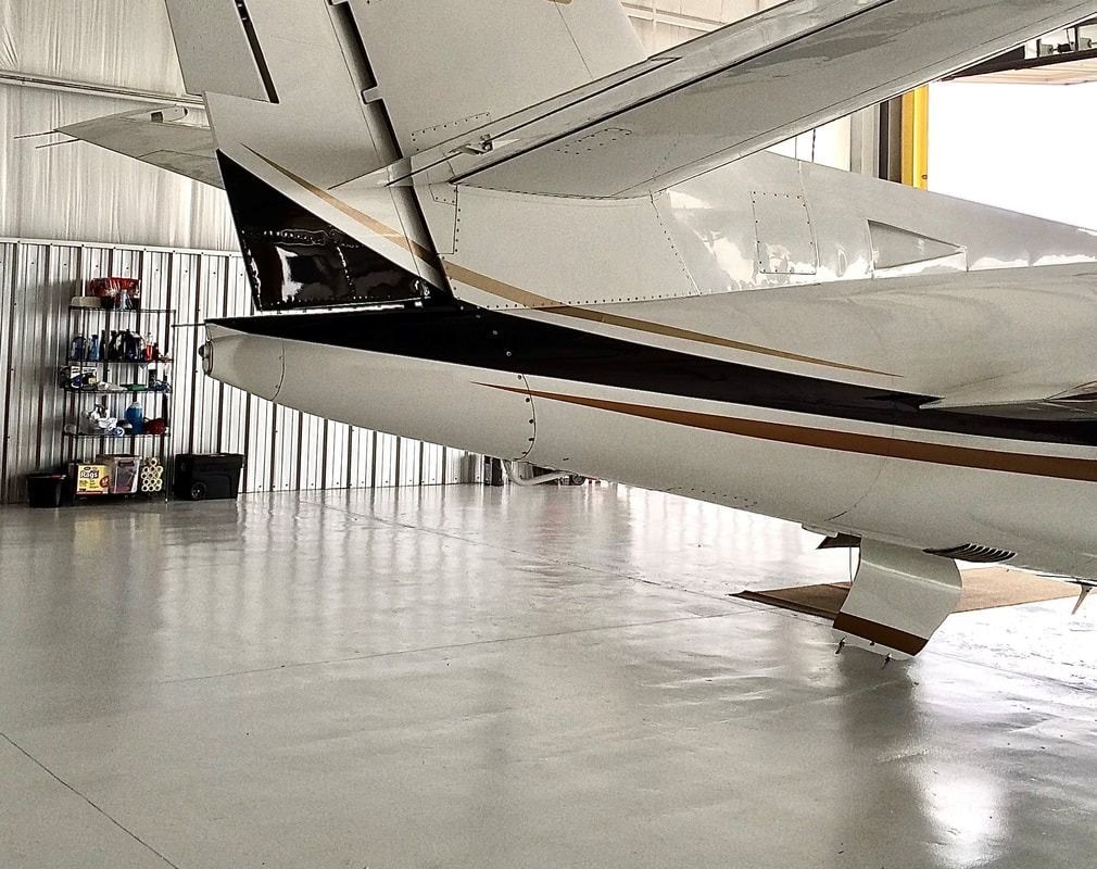 Close-up of a small white airplane in a hangar, showing its tail and wing