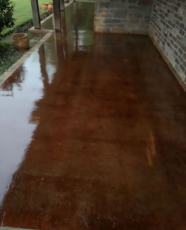 Wet brown concrete porch with reflections, beside a brick wall and potted plants