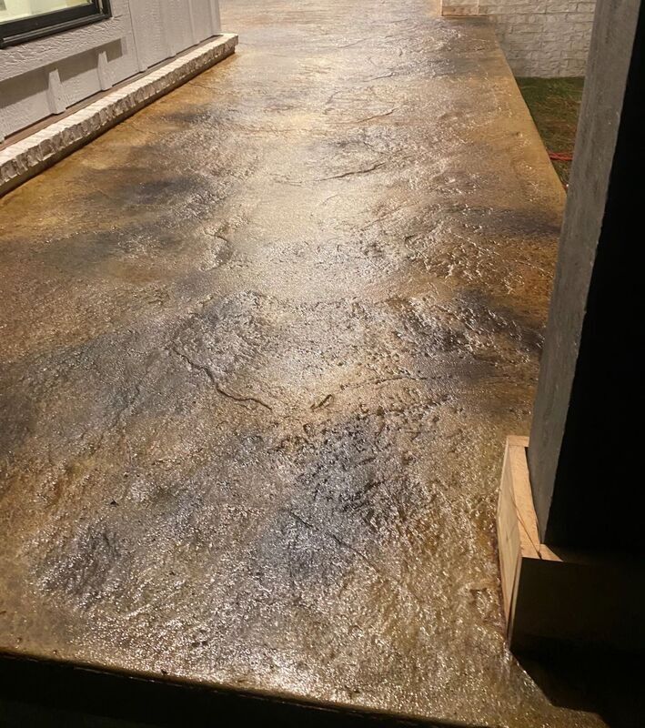 Wet concrete walkway beside a building, reflecting light and showing dark stains and cracks
