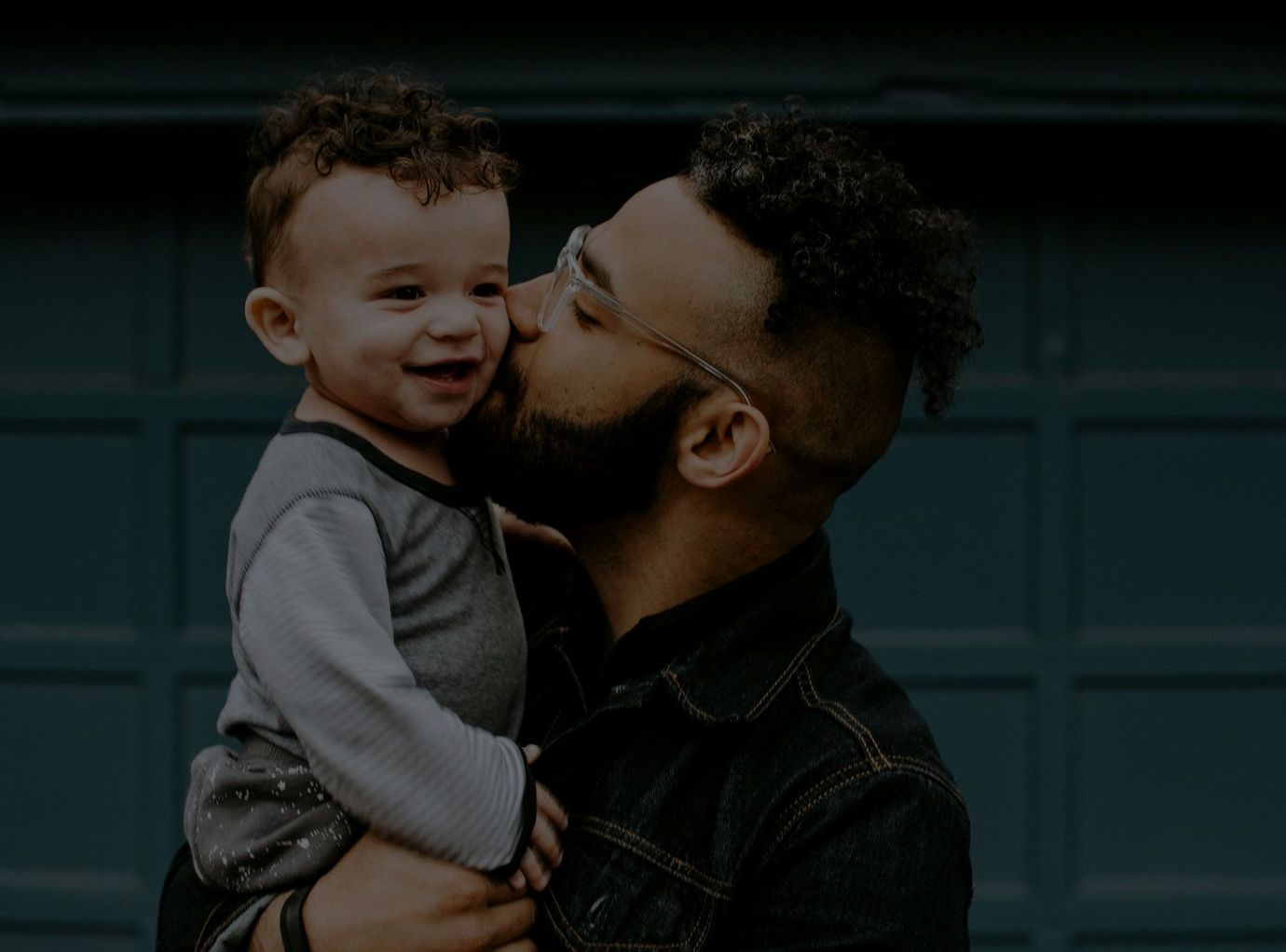 A father kissing his toddler son on the cheek.