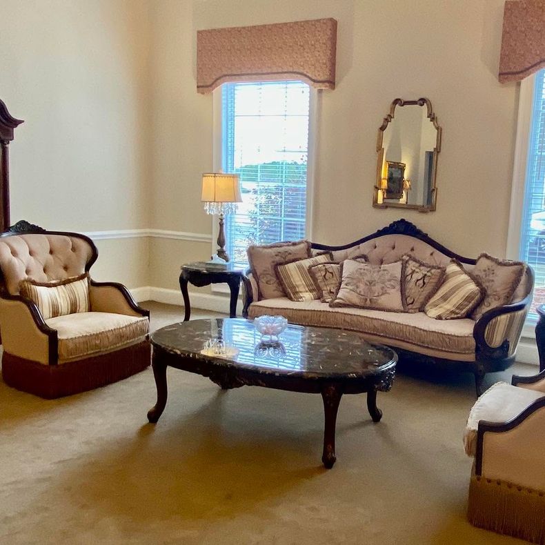 Elegant living room with beige sofa, armchairs, coffee table, lamp, and tall windows with valances.