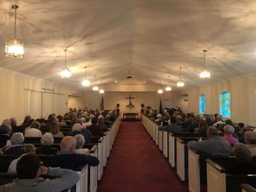 Wide church interior with seated congregation facing the altar along a red-carpeted center aisle.