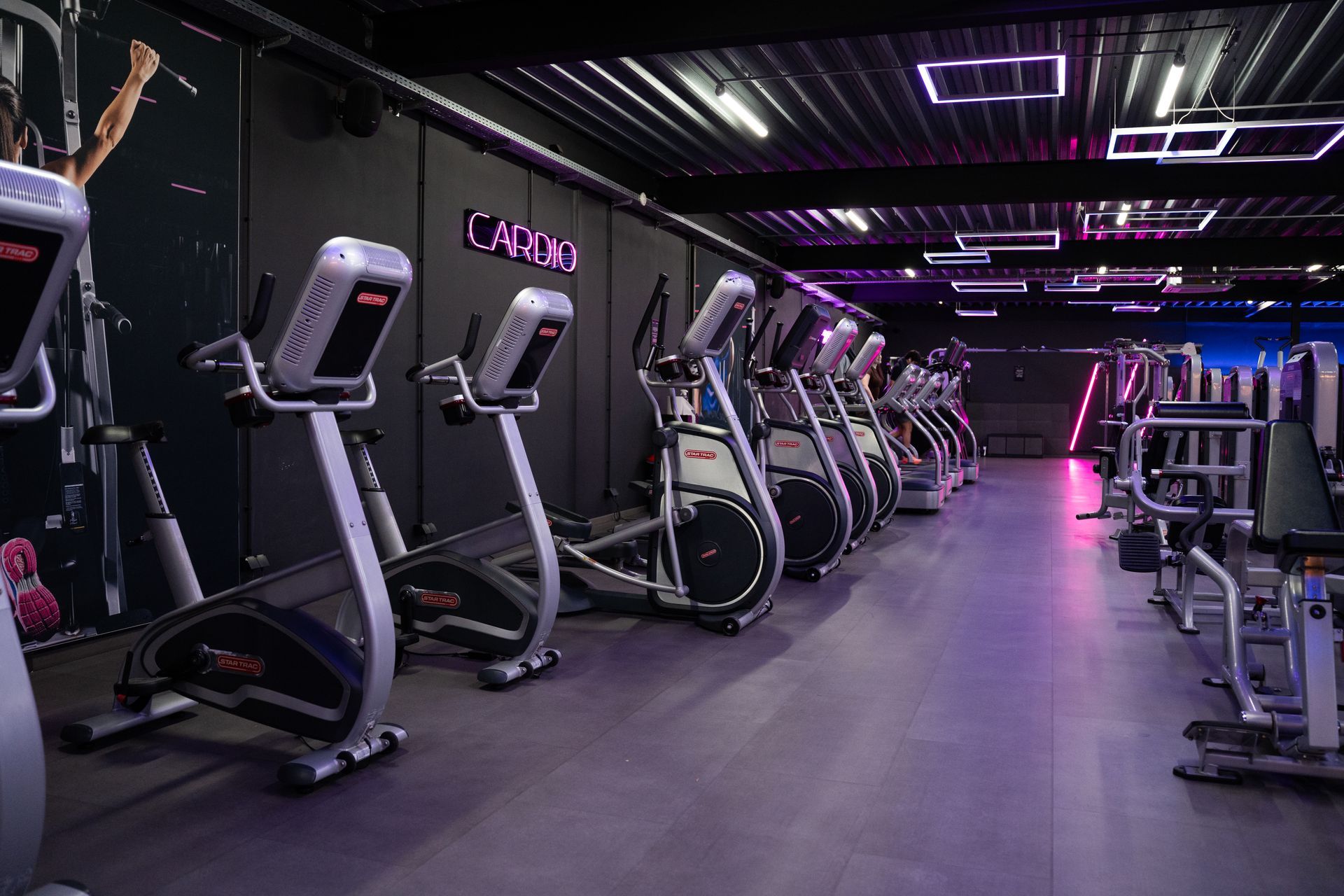 Lege sportschool met loopbanden en krachtapparaten onder paarse neonverlichting.