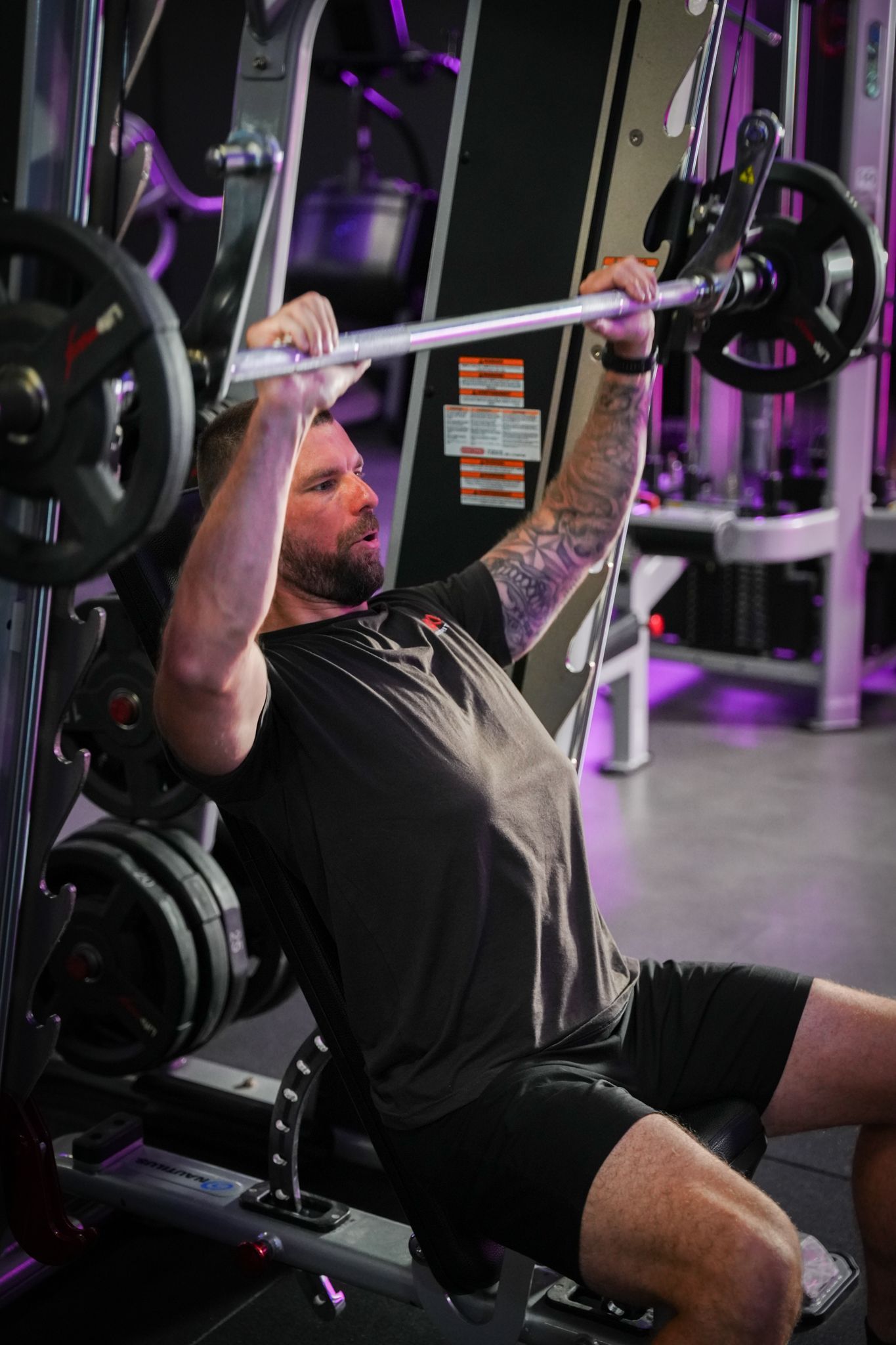 Een persoon doet lat pulldowns aan een kabelmachine in een sportschool met paarse verlichting.