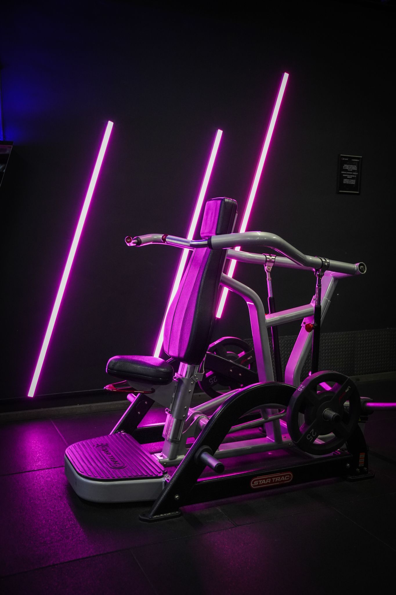 Fitnessapparaat verlicht door paarse neonlichten in een donkere, studio-achtige ruimte.