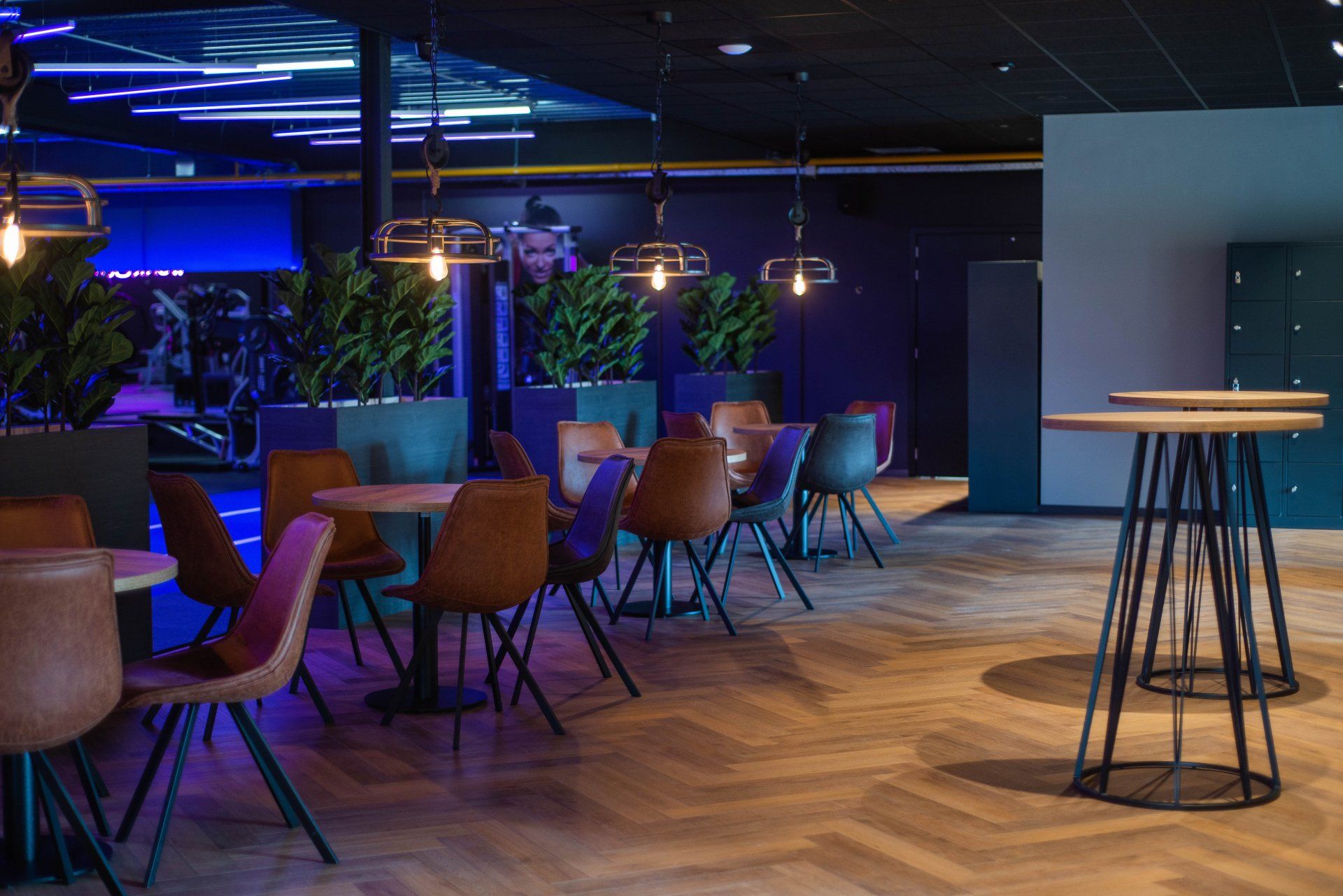 Moderne lounge met houten tafels en stoelen, blauwe neonverlichting en een hoge staande tafel op de voorgrond.