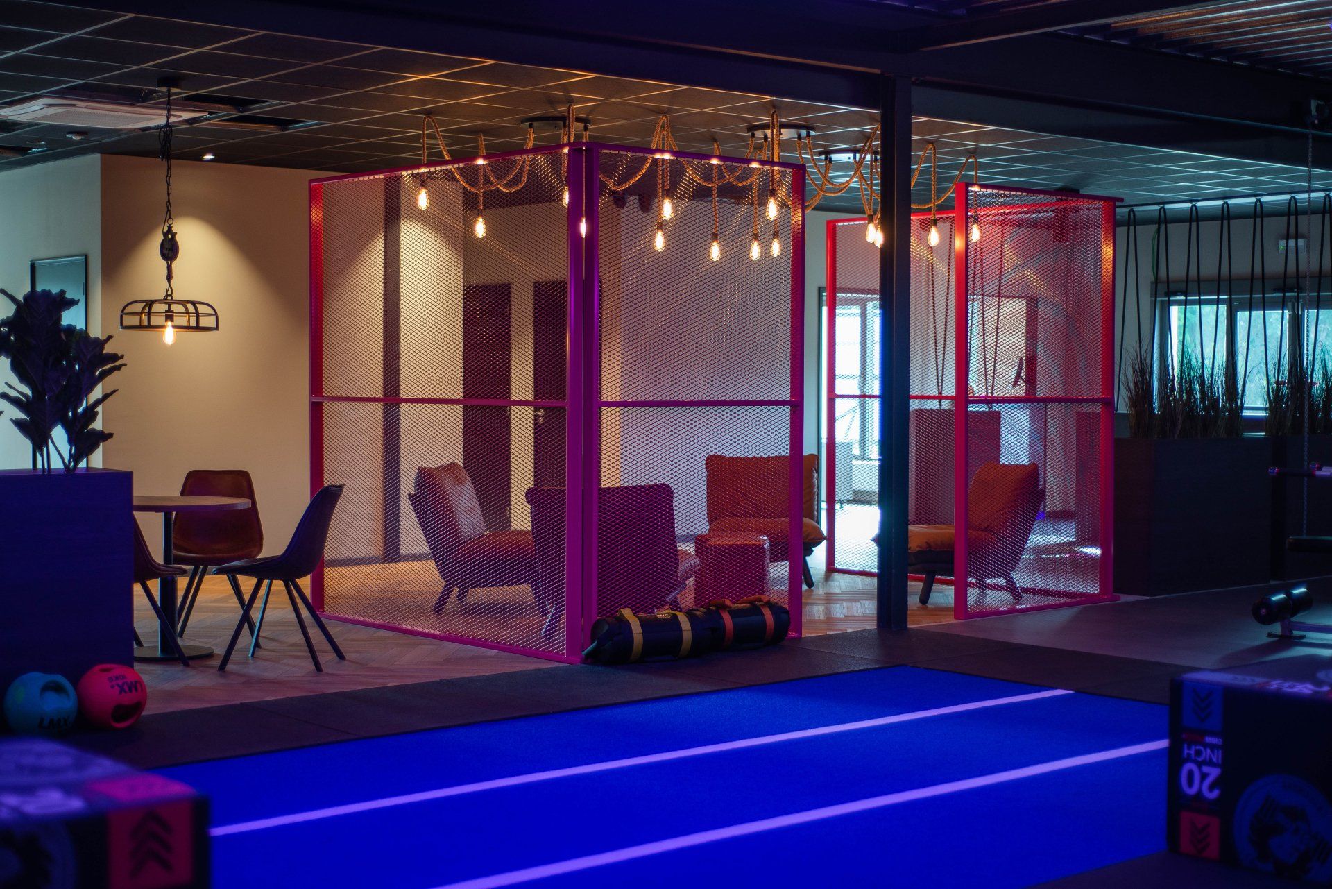 Binnengym met neonverlichting, omheinde trainingsruimte, matten en fitnessapparatuur in nachtsfeer.