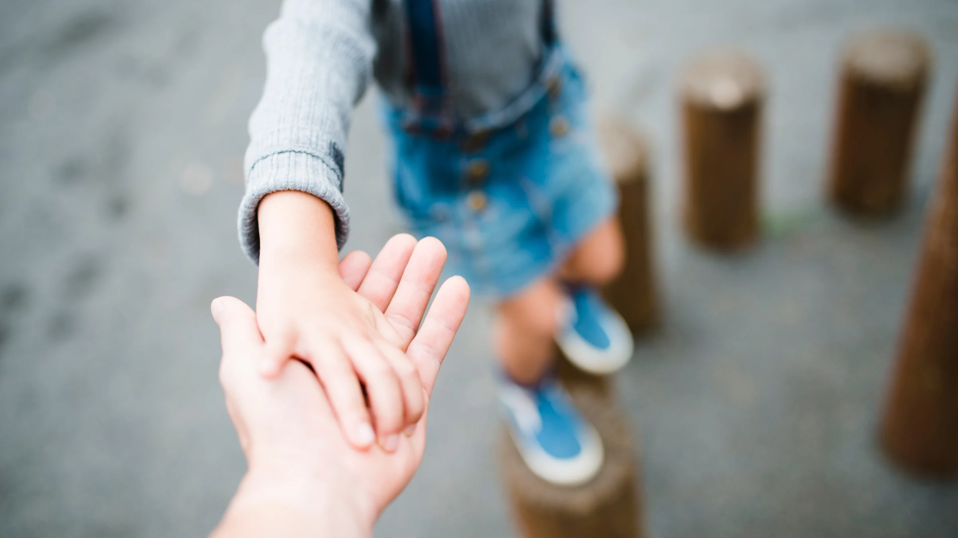 Hand holding child’s hand while walking across stepping stones outdoors