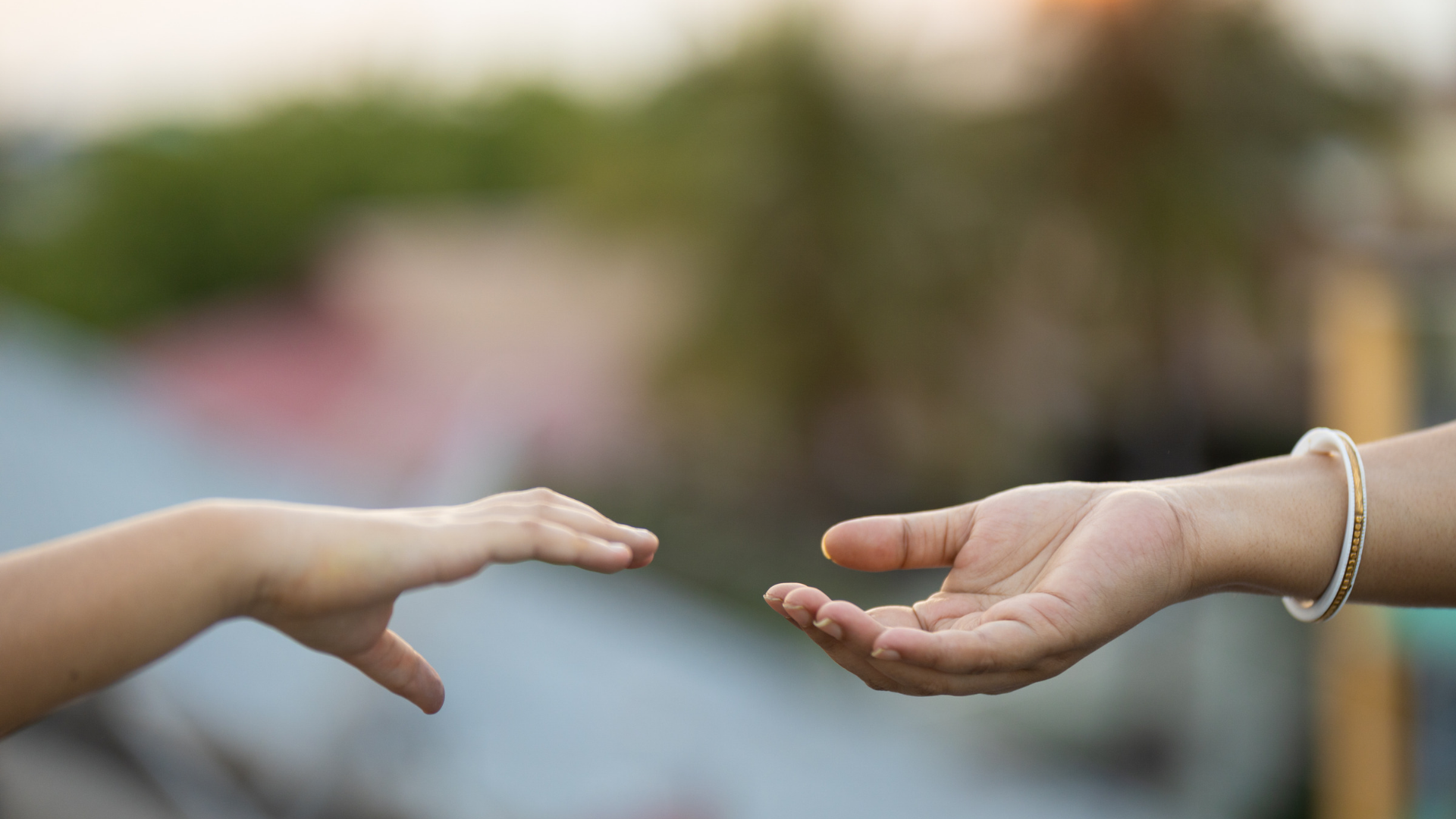 Two outstretched hands reaching toward each other against a blurred outdoor background