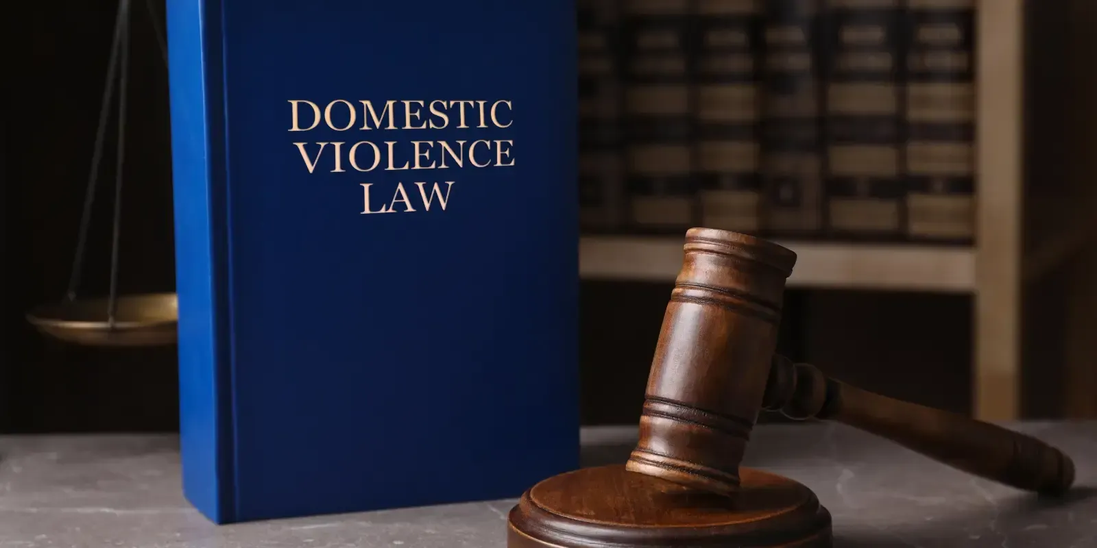 Blue “Domestic Violence Law” book beside a judge’s gavel on a desk with law books in the background