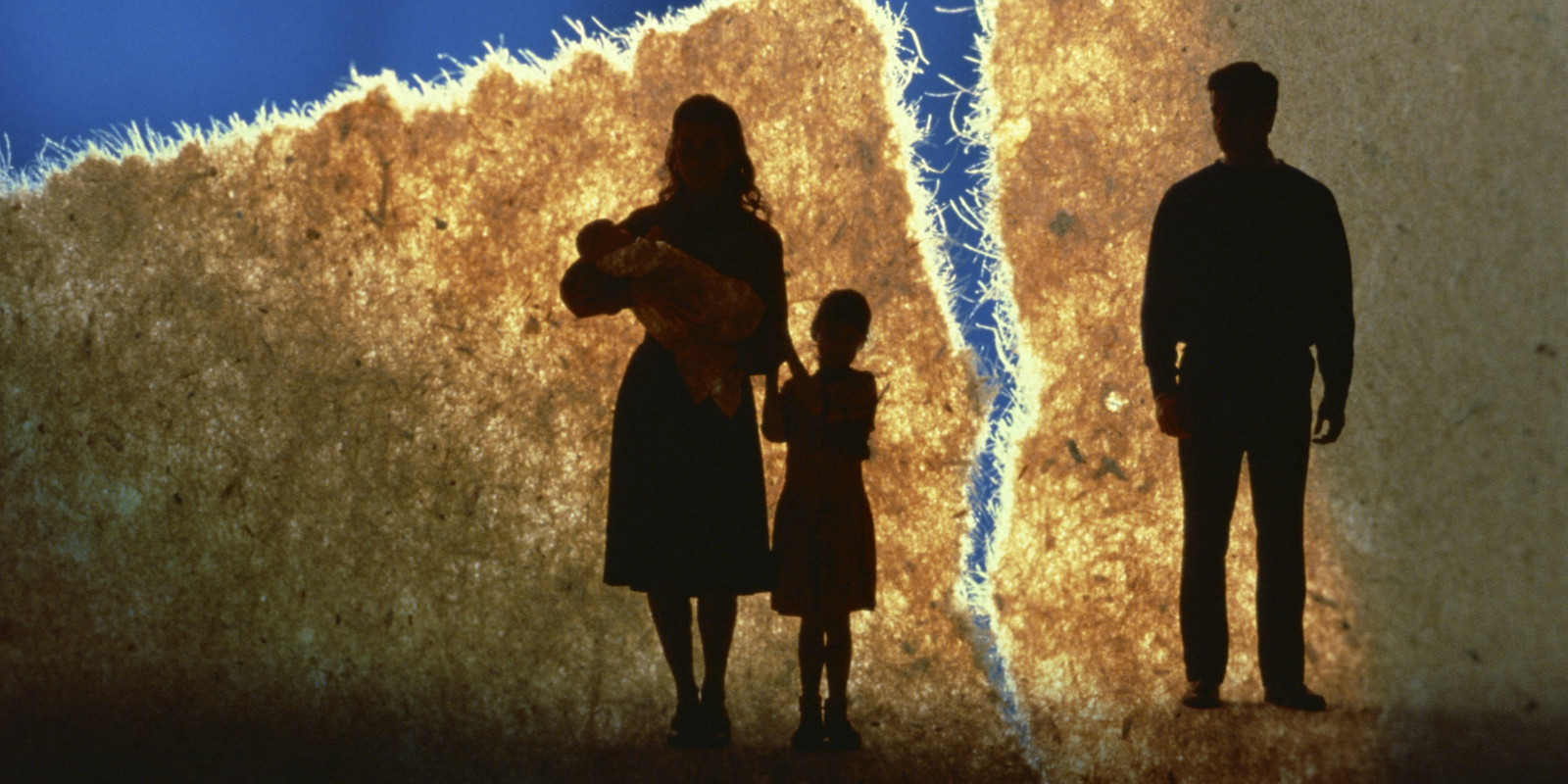 Three silhouetted people standing by a glowing crack in a wall at sunset