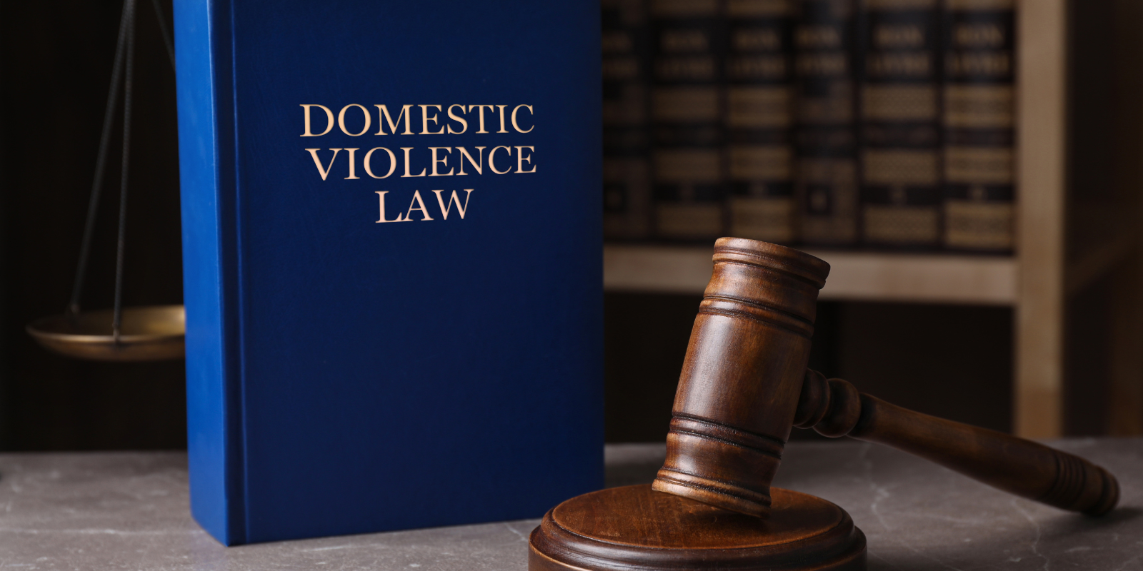 Blue “Domestic Violence Law” book beside a judge’s gavel on a desk with law books in the background