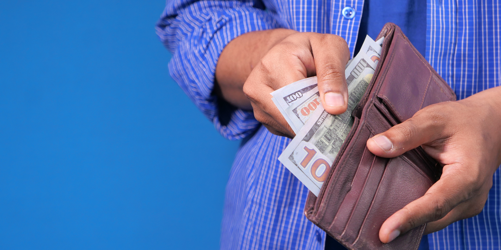 Hands holding cash and an open brown wallet against a blue background.