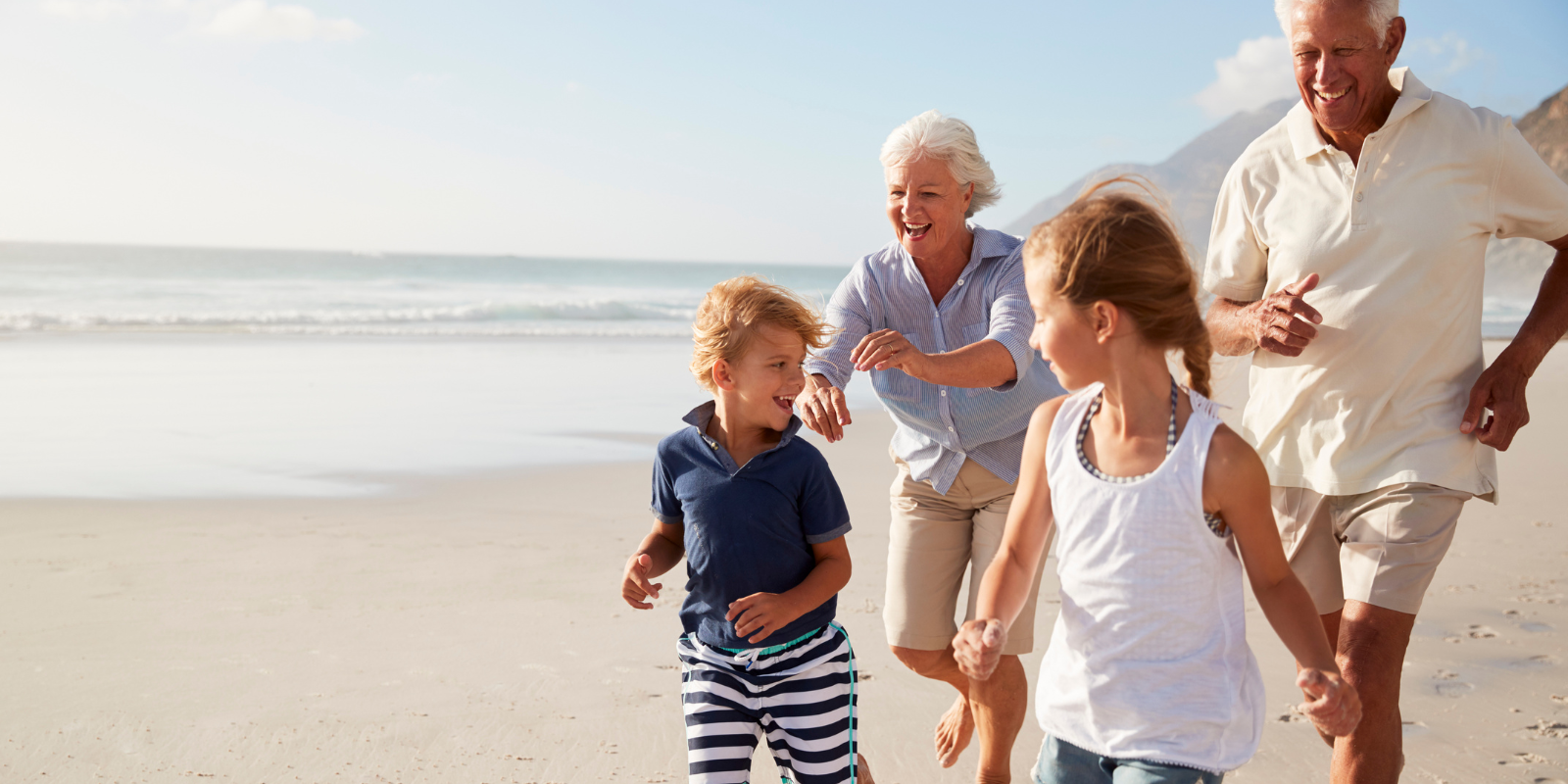 Family running barefoot on a sunny beach near the shoreline