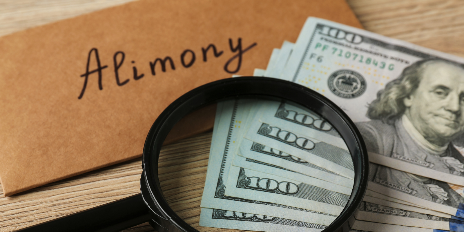 Alimony written on a folder beside U.S. dollar bills and a magnifying glass