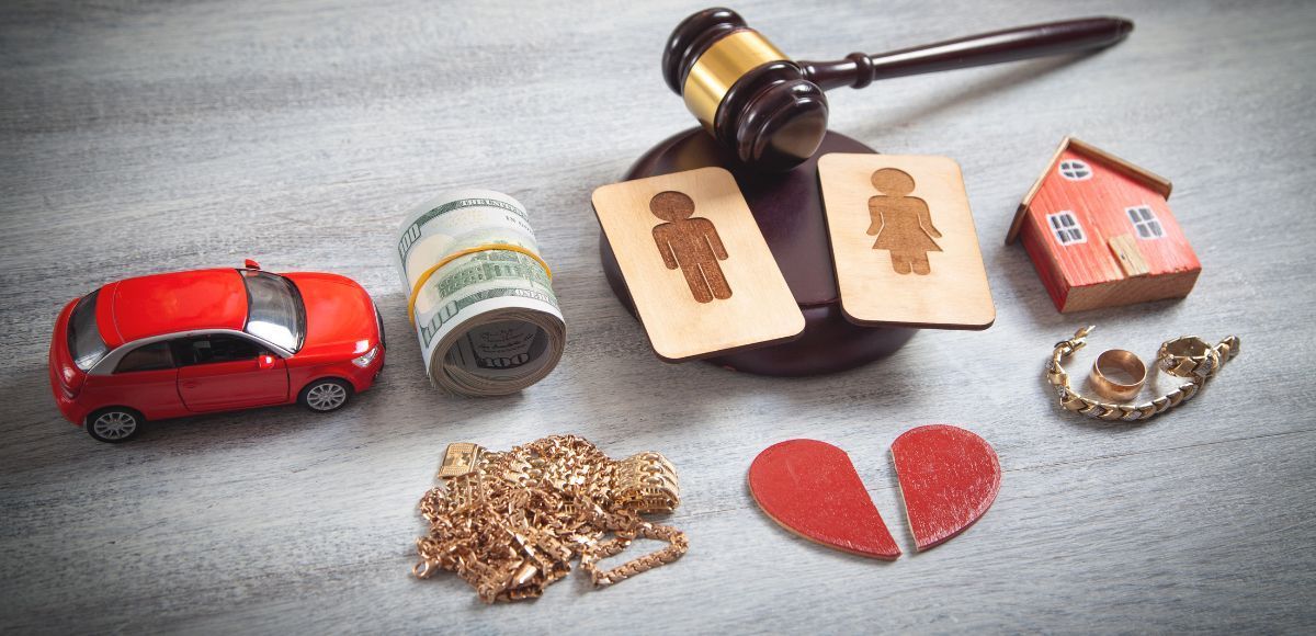 Divorce settlement symbols: gavel, toy car, ring, house, broken heart, and coins on gray surface