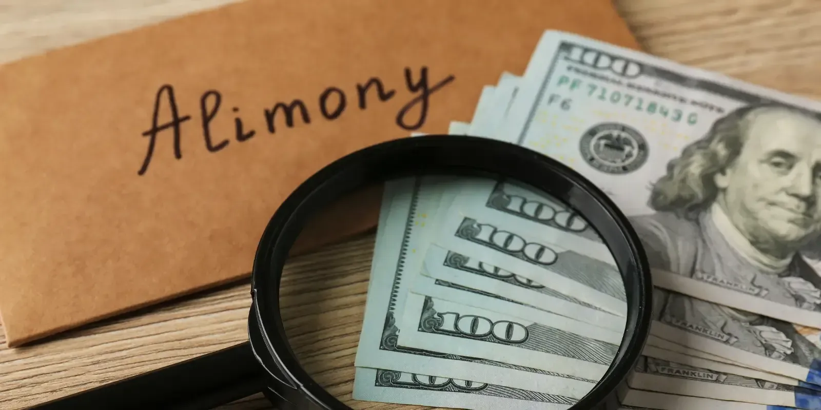Alimony written on a folder beside U.S. dollar bills and a magnifying glass