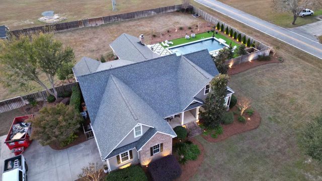 Aerial view of a large house with a pool and landscaping, including a driveway and a road.
