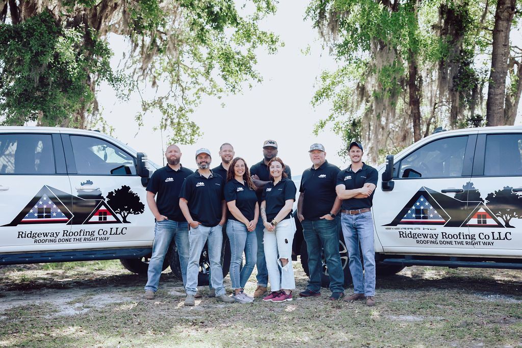 Group of people standing in front of two company trucks with logo. Trees in the background.