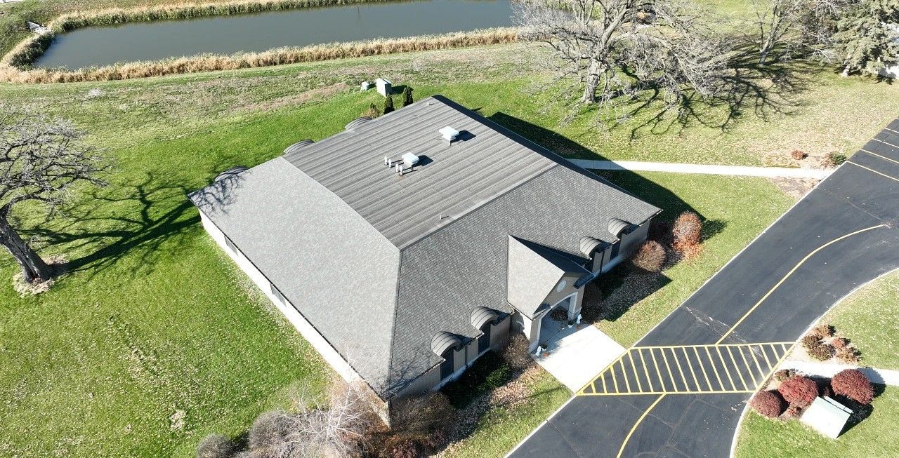 Aerial view of a gray-roofed house with a driveway, lawn, and a canal nearby.