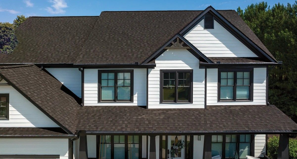 Two-story suburban house with brown shingle roof and white siding, seen from the front.