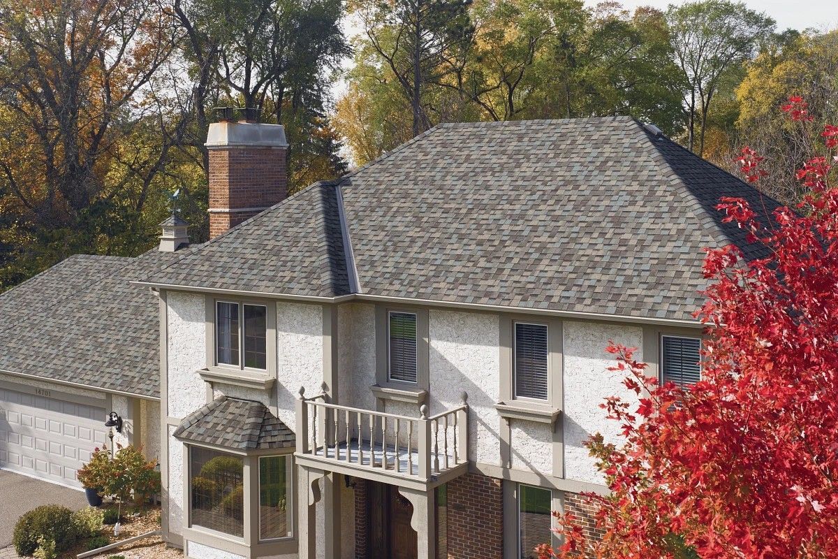 Two-story white house with gray roof and front balcony, framed by autumn trees and red foliage