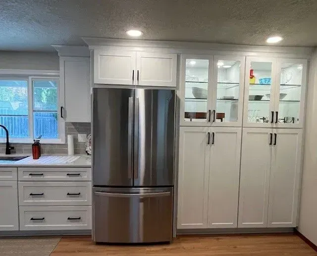 Bright white kitchen with stainless steel fridge, cabinets, and a window over the sink