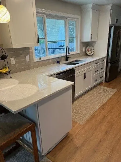 Bright kitchen with white countertops, sink under window, and wood floor runner.