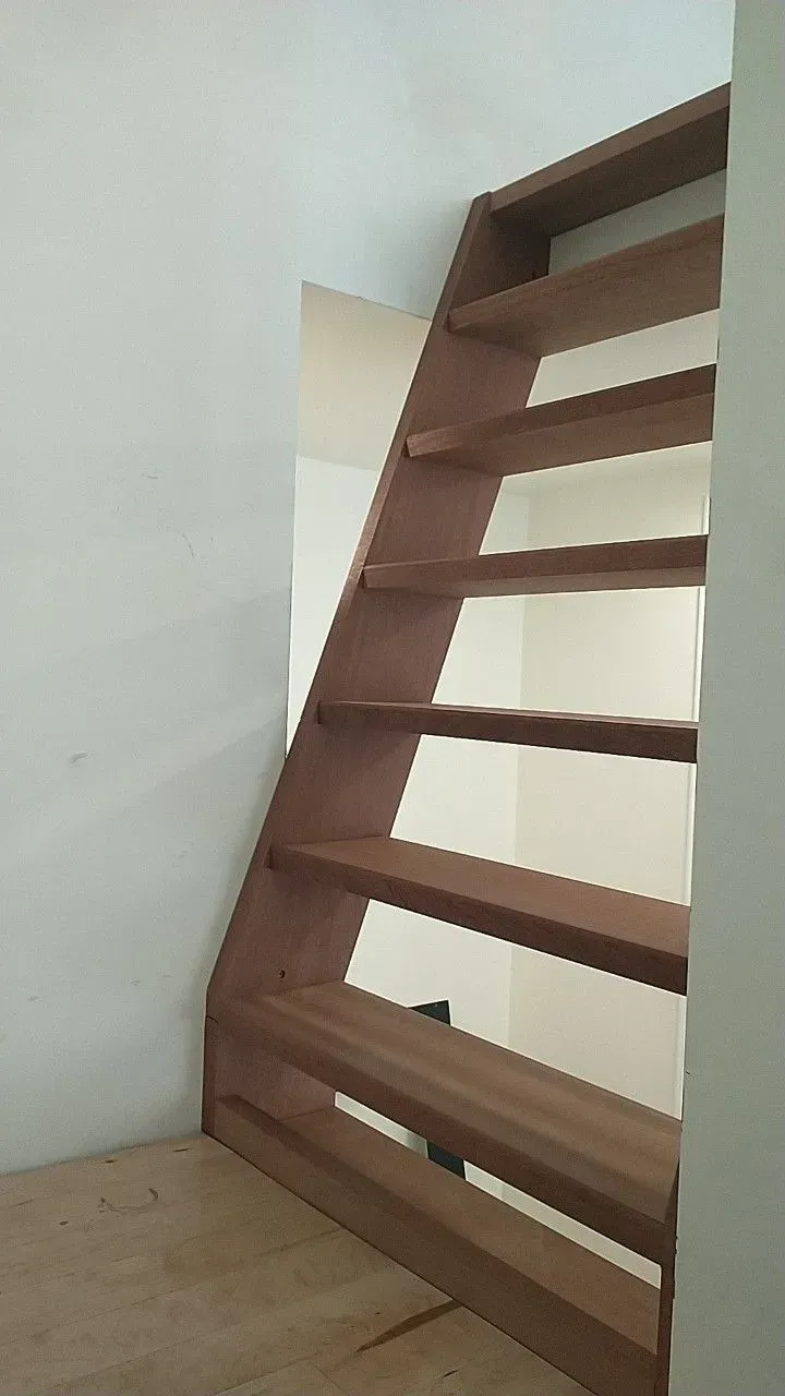 Wooden staircase with open risers against a white wall in a small interior space