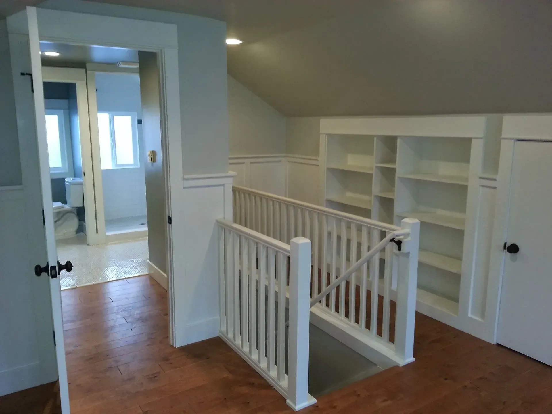 Bright loft hallway with white railings, built-in shelves, and wood flooring in an upstairs landing