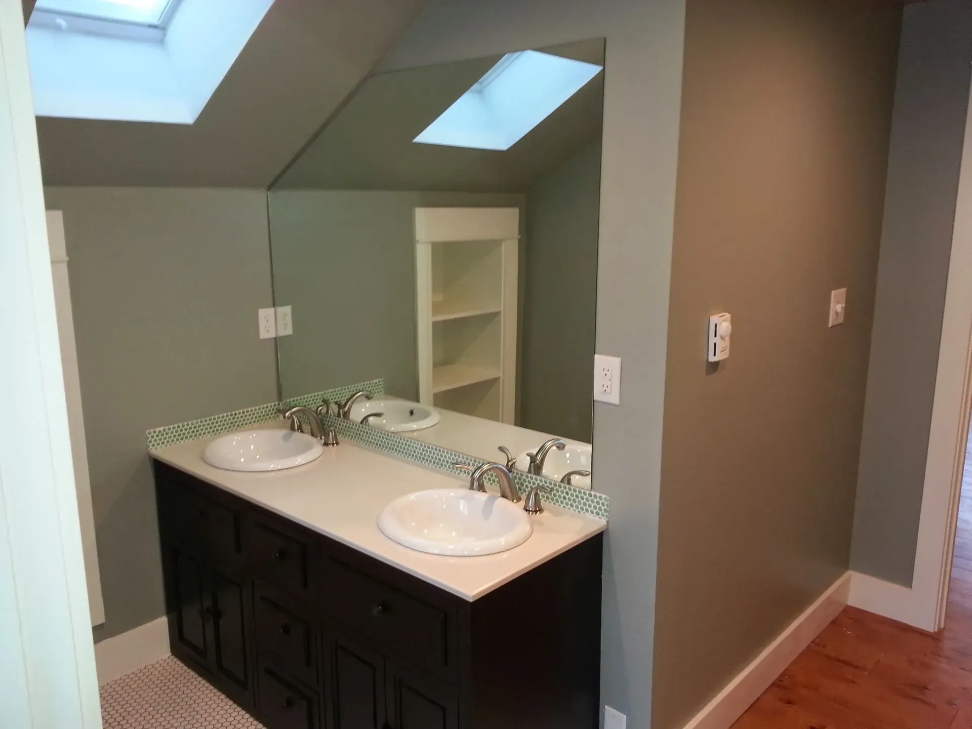 Bathroom vanity with double sinks, dark cabinets, and a large mirror under skylight windows