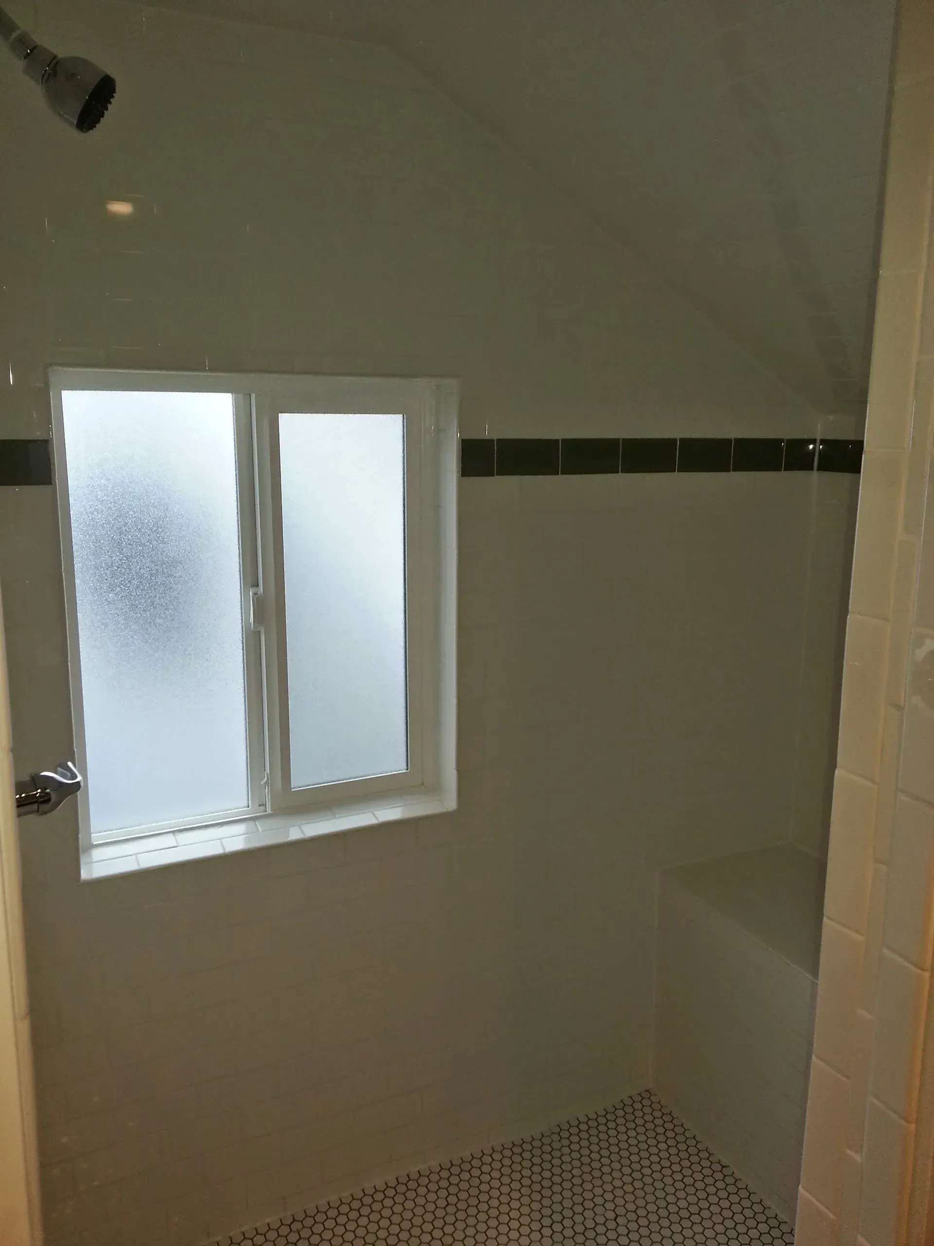 Small bathroom with frosted window, white tile walls, and patterned shower floor.