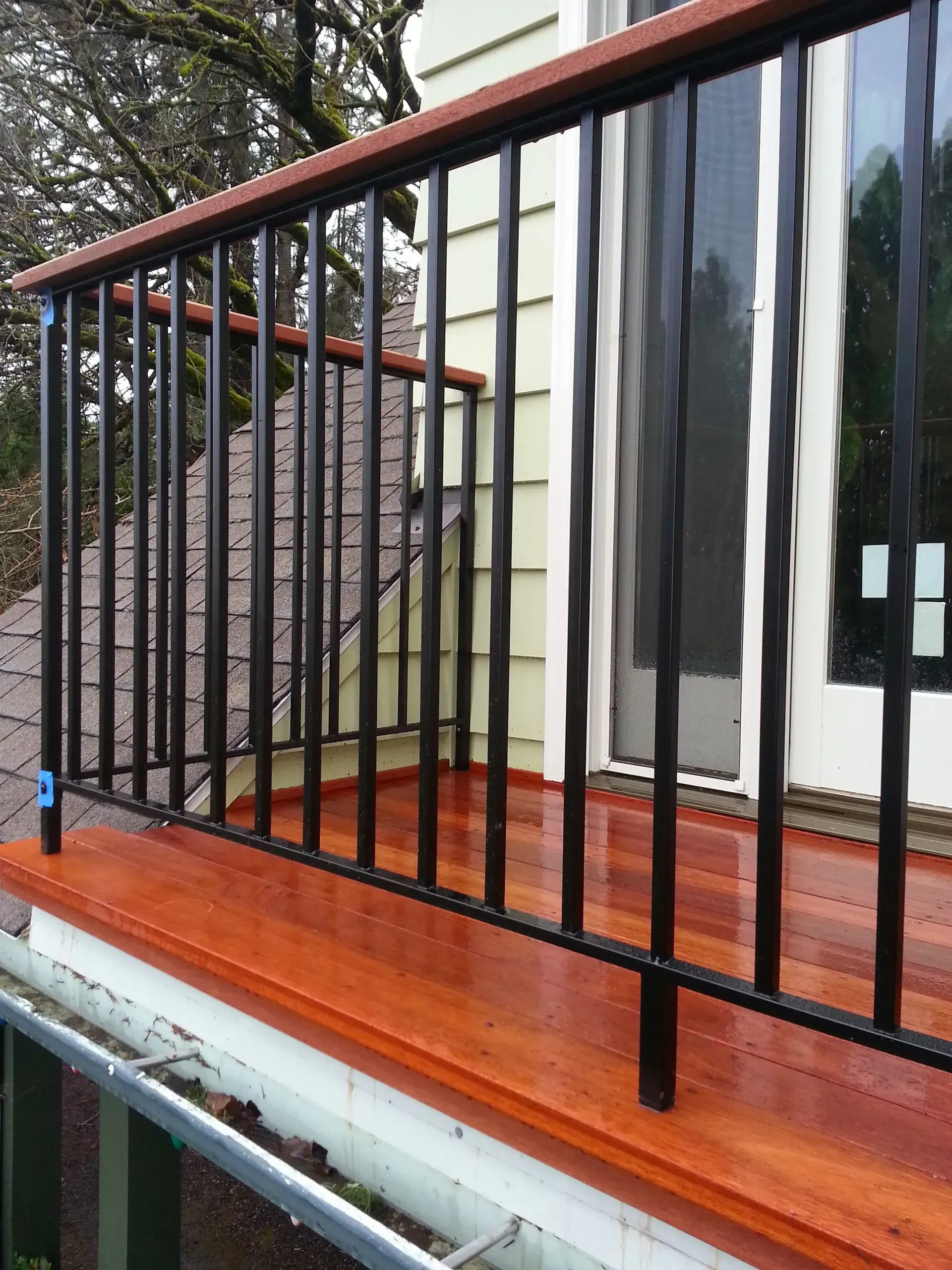 Black metal porch railing on a red wooden deck beside a house entrance