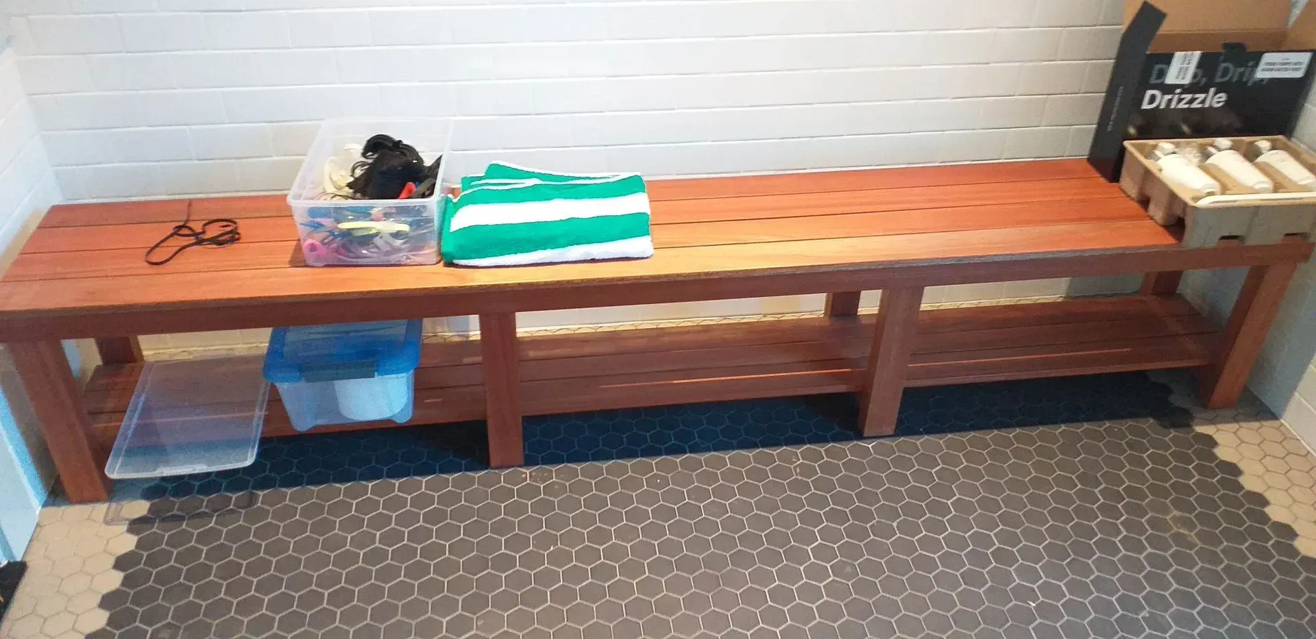 Wooden bench with shoes, a bag, and folded towels against a white brick wall