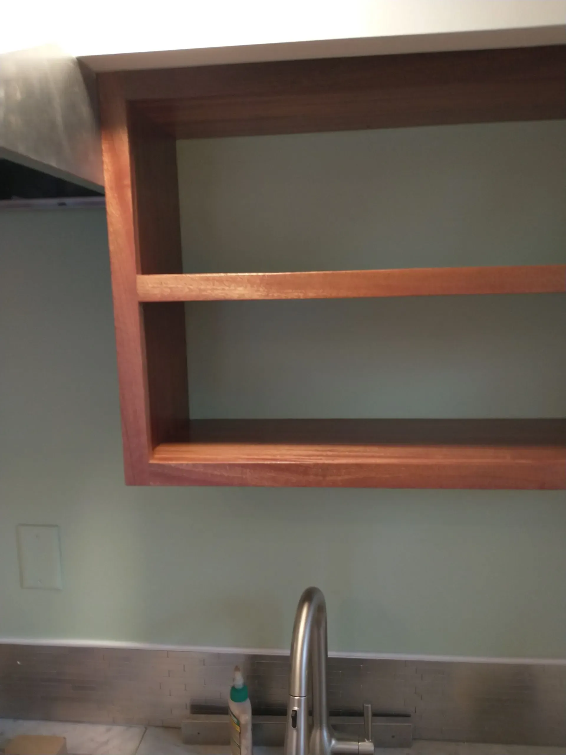 Wooden kitchen shelf above a sink and faucet against a pale green wall